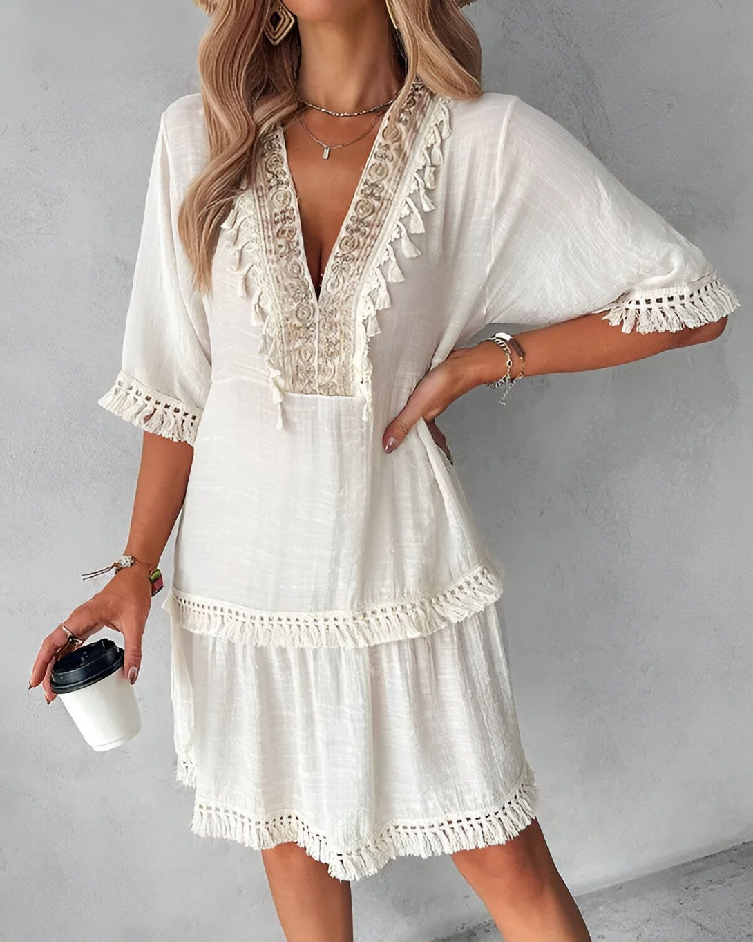 Une jeune femme porte une robe blanche courte à manches courtes. La robe est ouverte en V et possède des détails en dentelle. Elle porte également un collier et un bracelet.