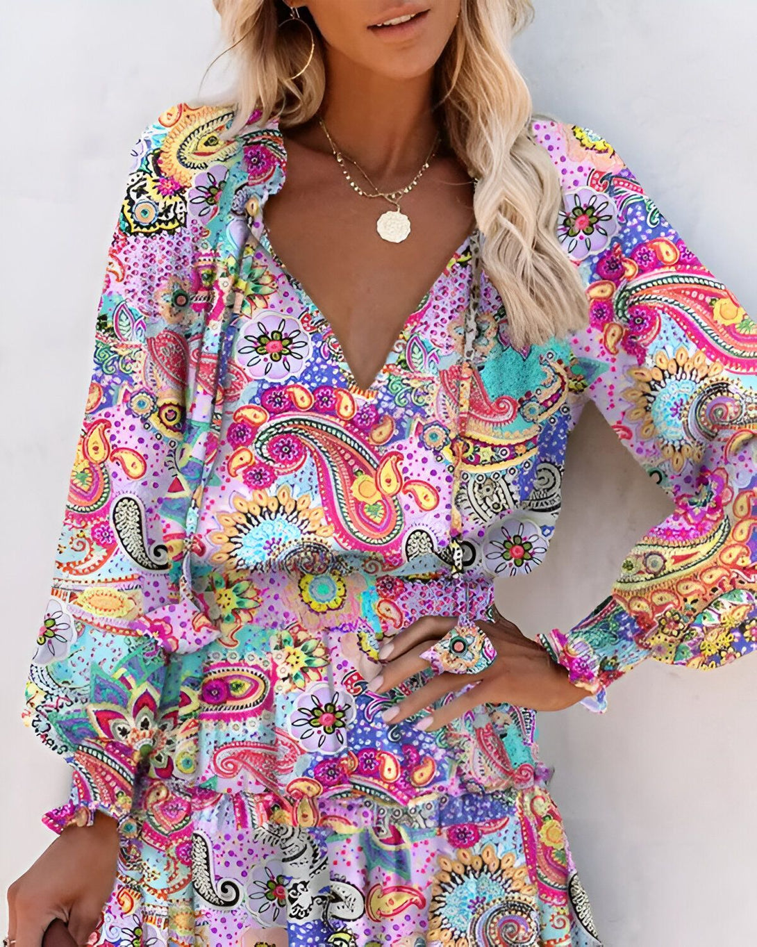 Une femme porte une robe colorée à motifs cachemire. La robe est décolletée en V et a des manches longues. La femme est blonde et porte un collier.