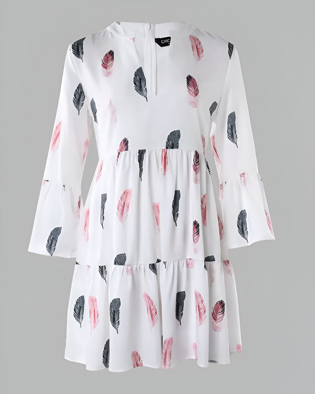 Une robe blanche à manches longues et à volants. La robe est imprimée de plumes roses, grises et noires.