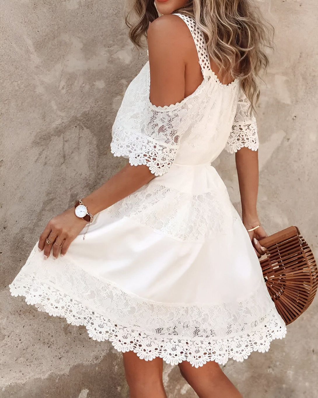 Une jeune femme porte une robe blanche en dentelle. La robe est courte et évasée, avec un décolleté en V et des manches courtes. La femme est blonde et porte un chapeau de paille marron. Elle est souriante et semble heureuse.