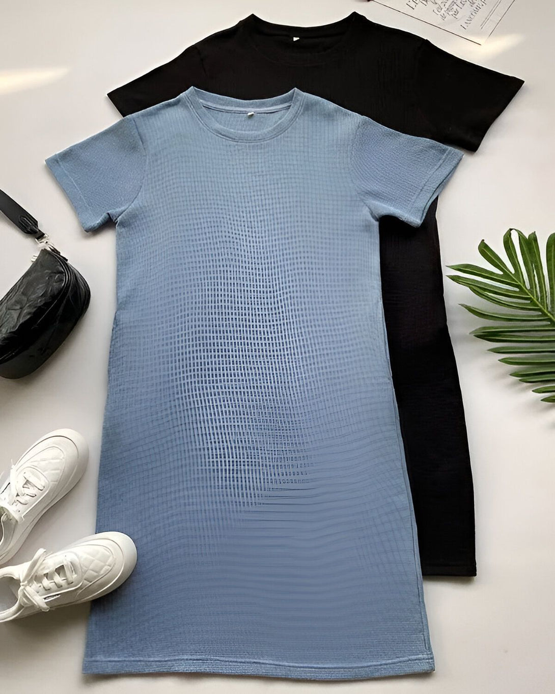 Une image de deux robes d'été, une bleue et une noire. Les robes sont toutes les deux à manches courtes et ont une coupe droite. La robe bleue est texturée et la robe noire est lisse. Il y a une paire de baskets blanches et un sac à main noir sur le côté gauche de l'image. Il y a une plante verte sur le côté droit de l'image.