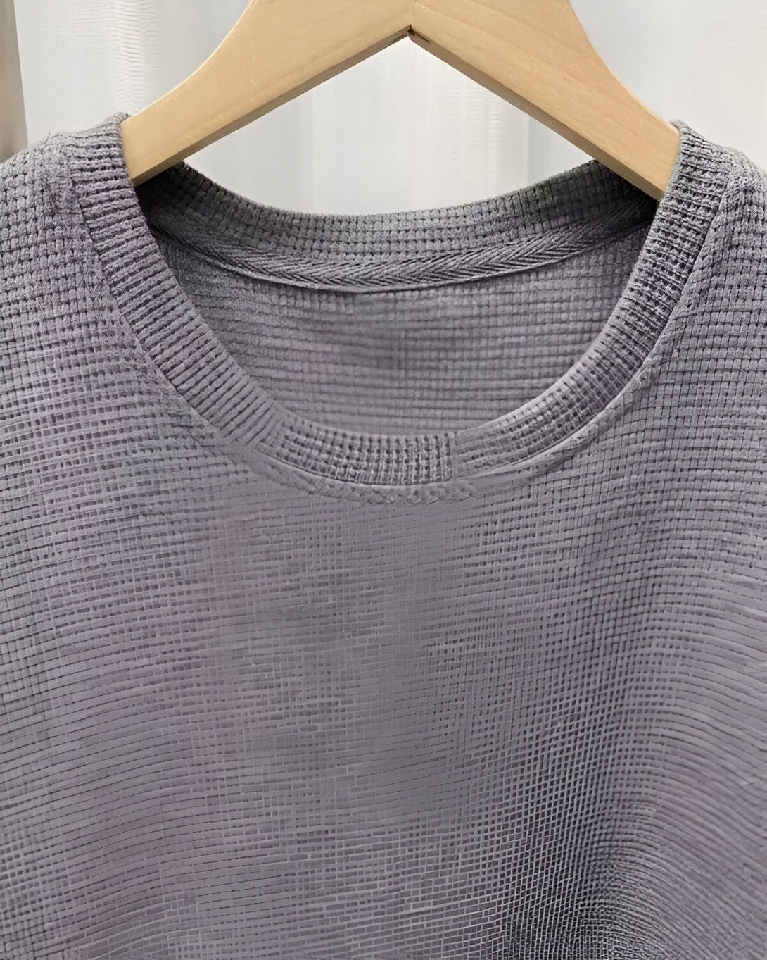 Une image d'un t-shirt gris chiné avec un col rond et des manches courtes, suspendu à un cintre en bois.