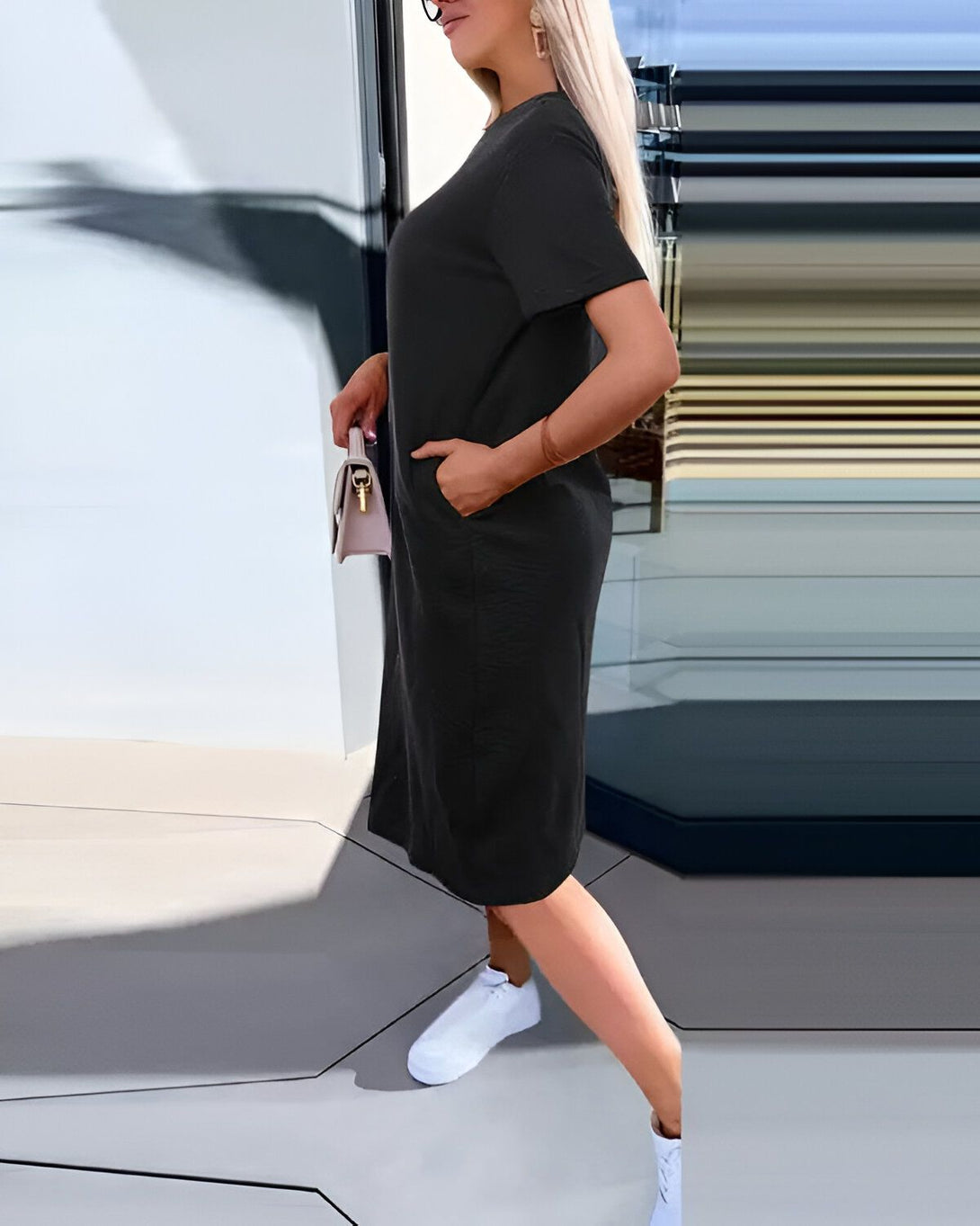 Une femme porte une robe noire décontractée avec des baskets blanches et un sac à main beige.