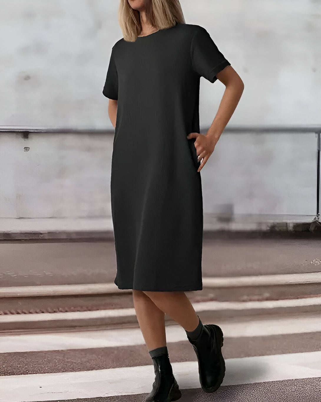 Une femme porte une robe noire mi-longue à manches courtes. Elle est associée à des bottines noires.