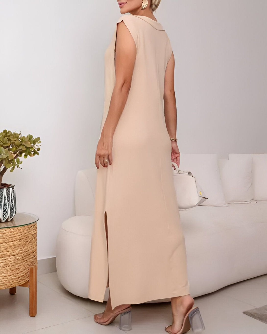 Une femme portant une longue robe beige sans manches avec une fente sur le côté. Elle est vue de dos.