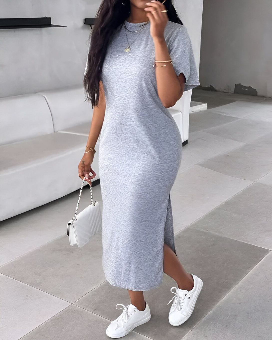 Une femme porte une robe longue grise en jersey avec des baskets blanches et un sac à main blanc.