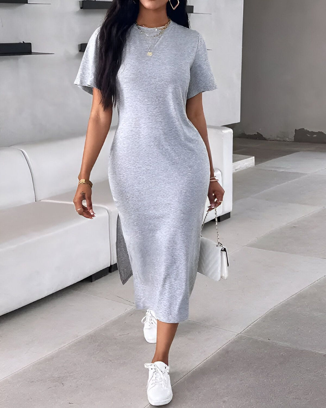 Une femme porte une robe longue grise en jersey, des baskets blanches et un sac à main blanc.