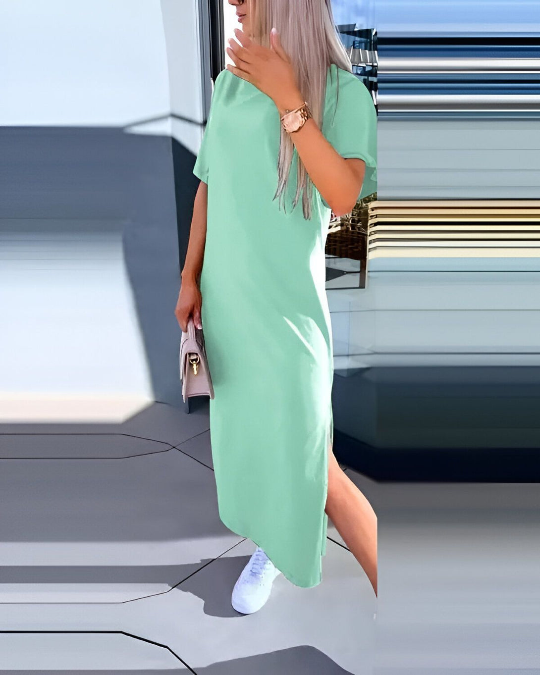Une femme porte une robe longue vert menthe fendue sur le côté. Elle a des baskets blanches et un sac à main beige.