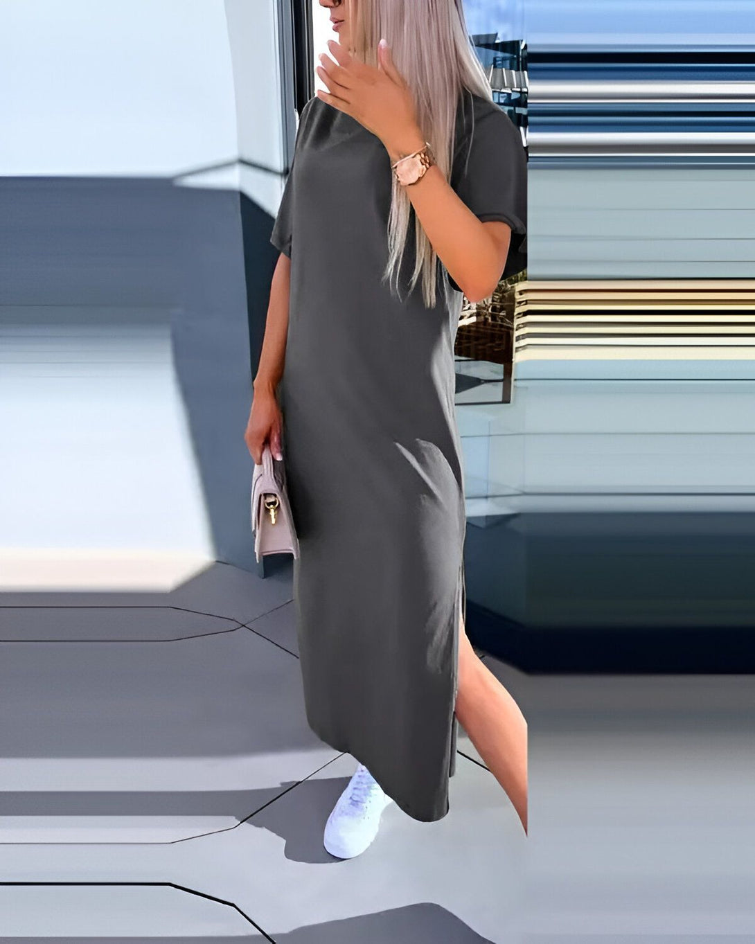 Une femme porte une robe longue gris foncé avec des manches courtes. La robe est fendue sur les côtés. Elle porte des baskets blanches et un sac à main rose.
