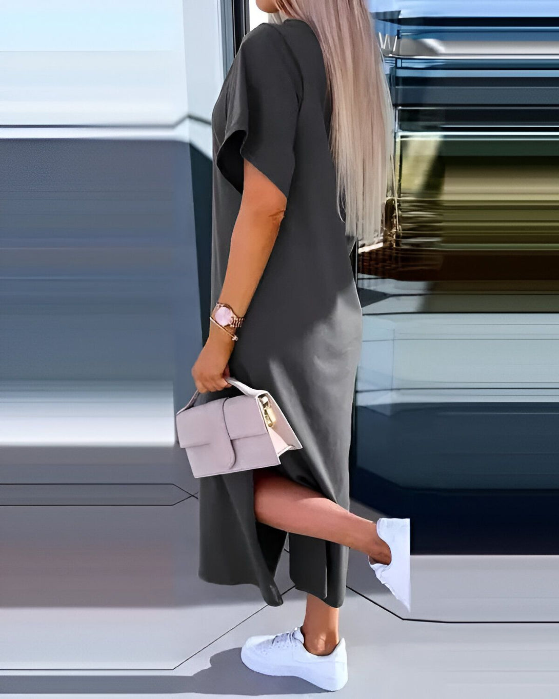 Une femme porte une robe longue gris foncé avec des baskets blanches et un sac à main beige.