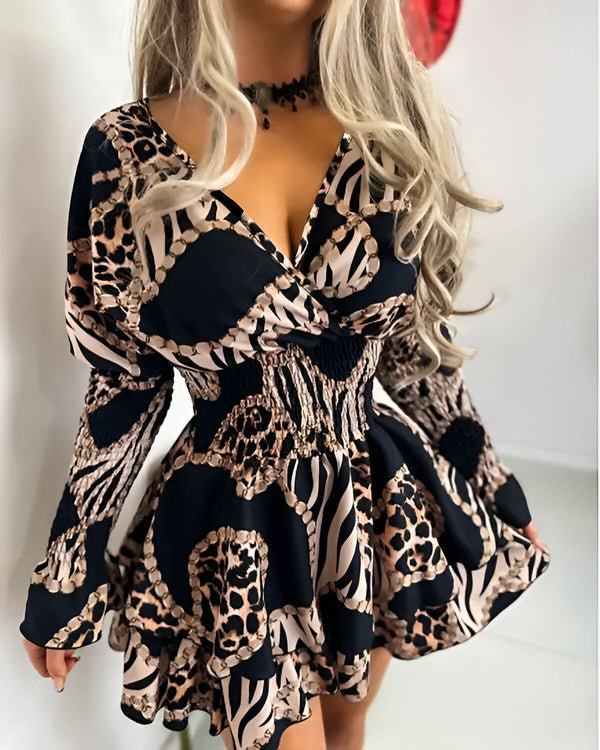 Une femme porte une robe noire et marron à motifs léopard et zèbre. La robe est cintrée à la taille et évasée au niveau des hanches. Elle a un décolleté en V et des manches longues. La femme est blonde et porte un collier noir. Elle est debout et regarde vers la caméra.