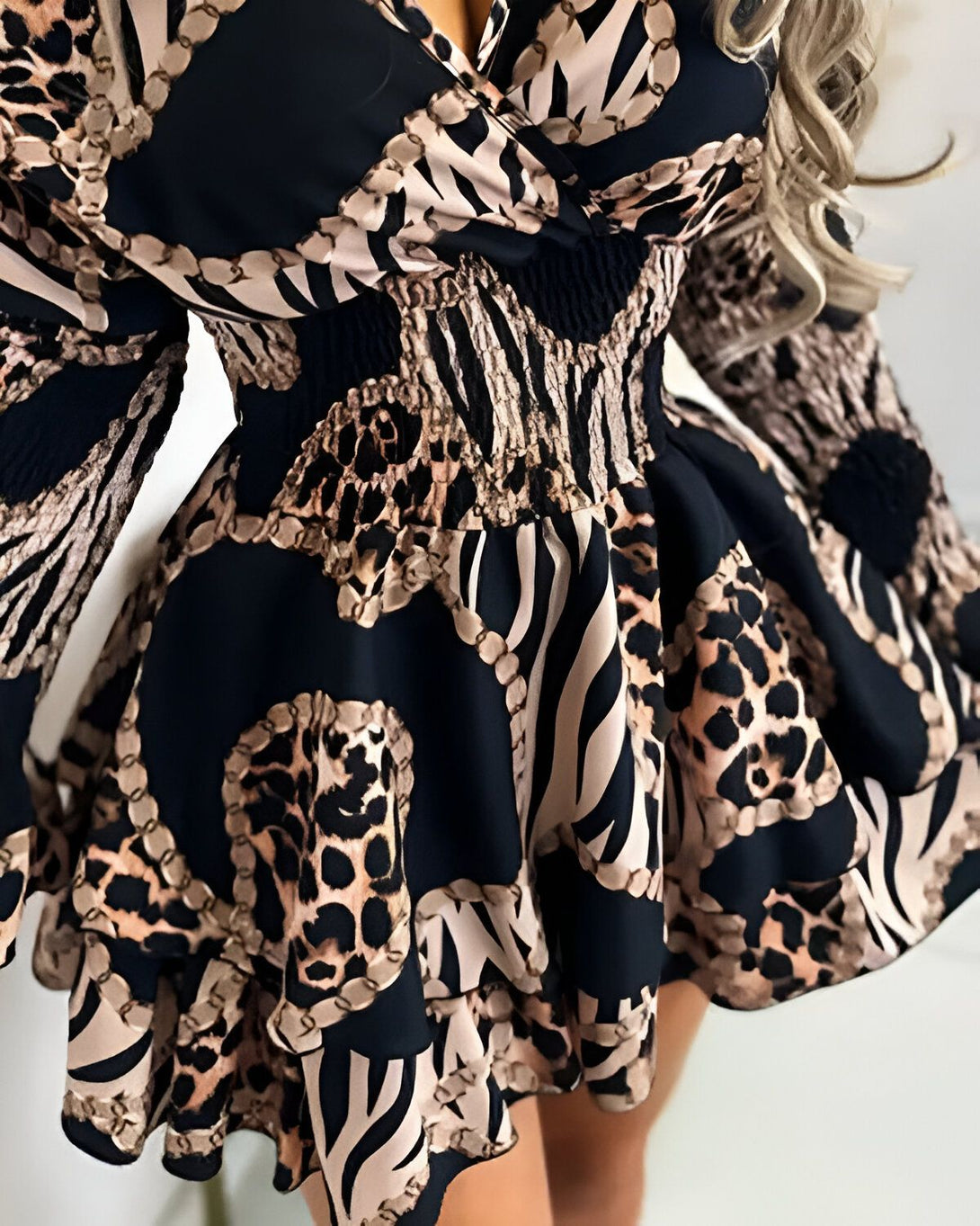 Une femme porte une robe noire et marron. La robe est cintrée à la taille et évasée au niveau des hanches. Elle est imprimée d'un motif léopard et de chaînes. La femme a les cheveux longs et blonds. Elle est maquillée et porte des talons hauts.