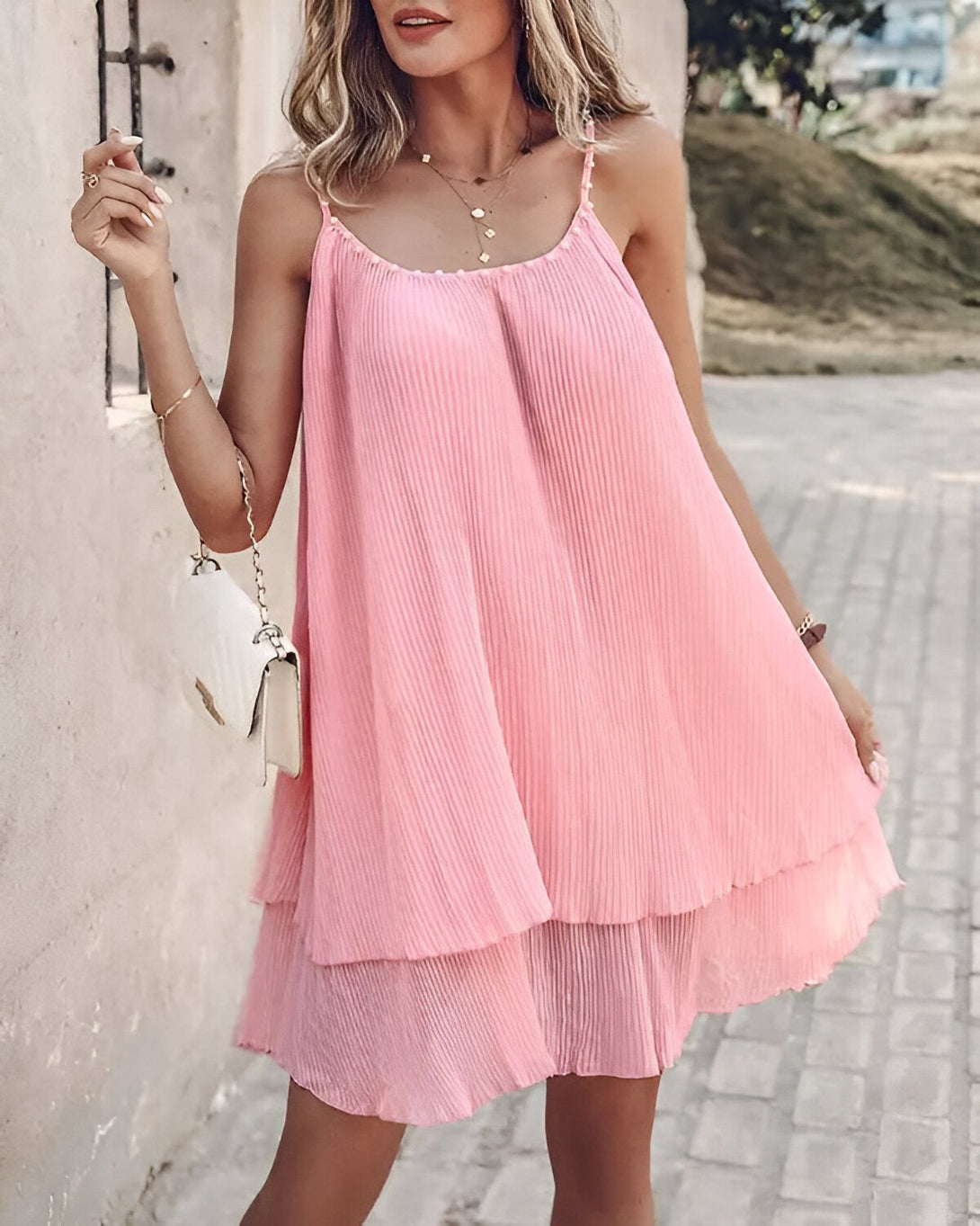 Une jeune femme portant une robe rose plissée courte avec des bretelles fines.