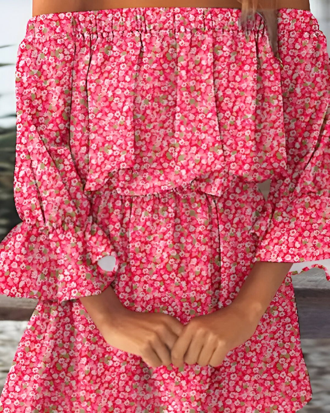 Une jeune femme porte une robe rose à fleurs. La robe est courte et a un volant au niveau de la poitrine. Les manches sont bouffantes et l'encolure est Bardot.