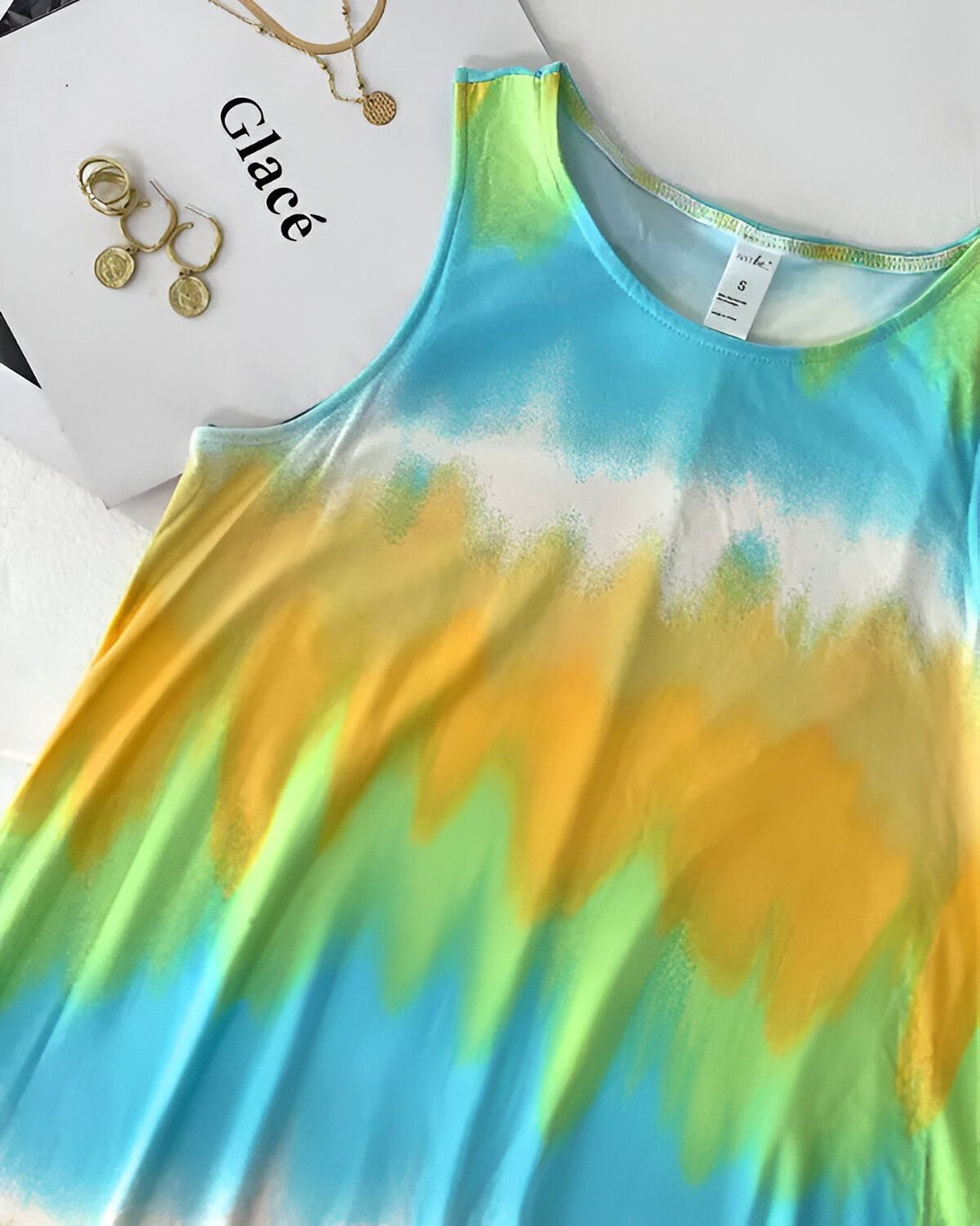 Une image d'une robe tie-dye aux couleurs vives. La robe est jaune, verte et bleue. Il y a des bijoux à côté de la robe.