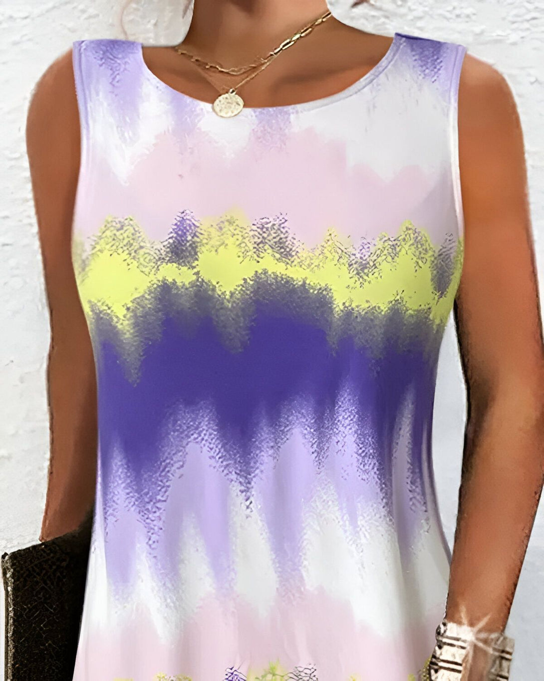 Une femme porte une robe débardeur blanche, rose et violette. La robe est sans manches et a une encolure ronde. La femme est vue de face et porte un collier.