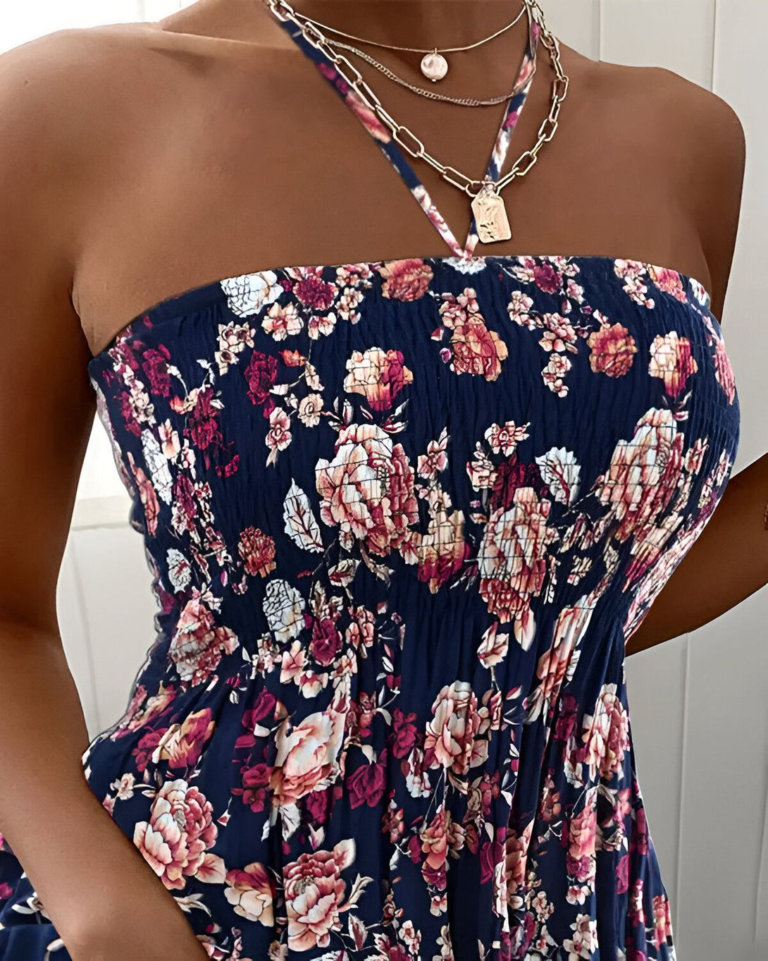 Une jeune femme porte une robe bustier à fleurs. La robe est bleu marine avec des fleurs roses et blanches. Elle porte également un collier avec un pendentif en forme de pièce de monnaie.