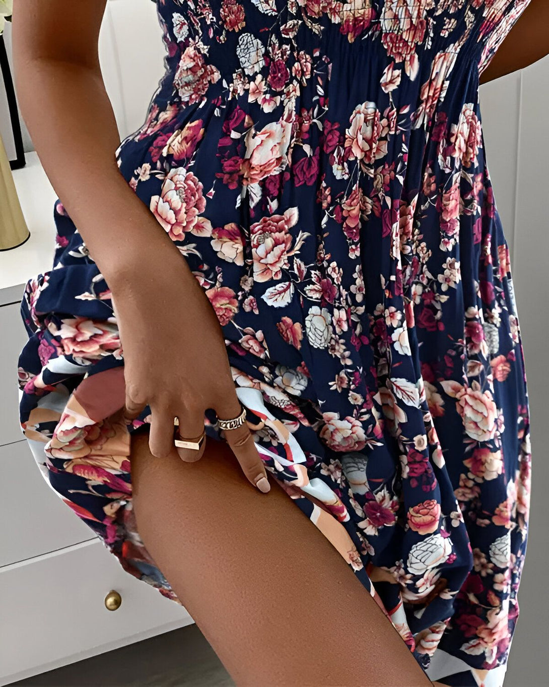 Une jeune femme porte une robe fleurie bleue et blanche. Elle est debout, la main sur la cuisse.