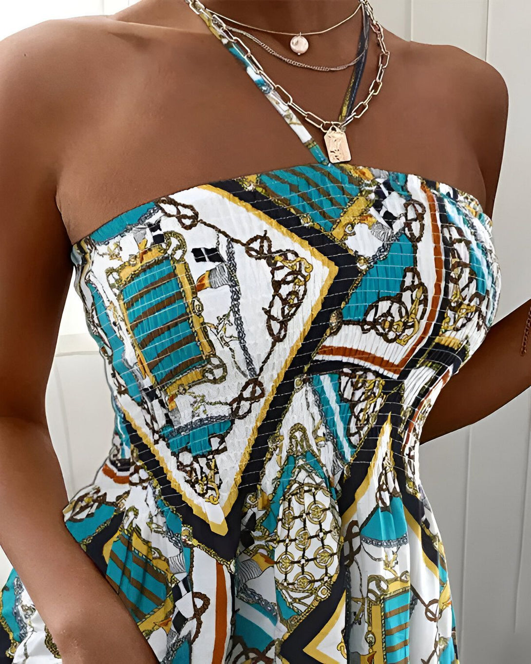 Une femme porte un haut court et une jupe assortis. L'ensemble est de couleur turquoise et présente un imprimé de chaînes et de médaillons. La femme est également porte un collier doré.