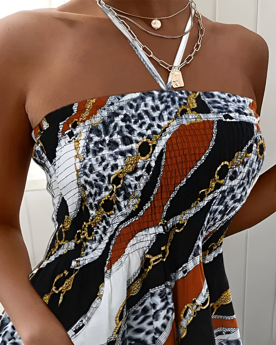 Une femme porte une robe bustier à imprimé chaîne. La robe est marron, noire et blanche. Elle porte également un collier avec un pendentif en forme de pièce de monnaie.