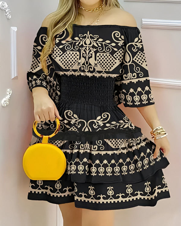 Une jeune femme porte une robe noire et beige à motifs ethniques. La robe est courte et évasée, avec un décolleté épaules nues. La femme porte également un sac à main jaune et des sandales noires.