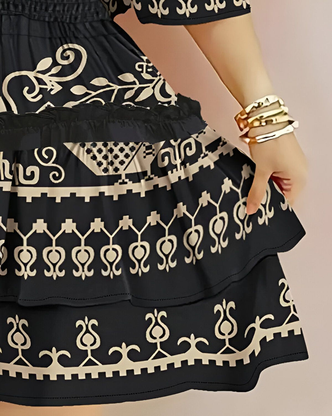 Une femme porte une robe noire et blanche à motifs. La robe est courte et évasée, avec un volant en bas. La femme a les cheveux longs et noirs et porte des bracelets dorés.