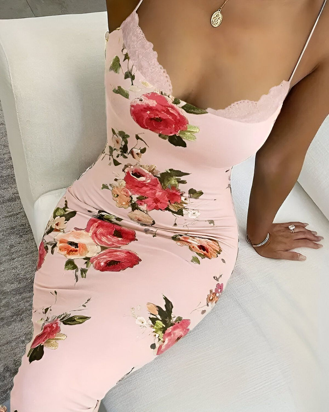Une femme porte une robe rose à fines bretelles. La robe est fleurie et possède un décolleté en V.