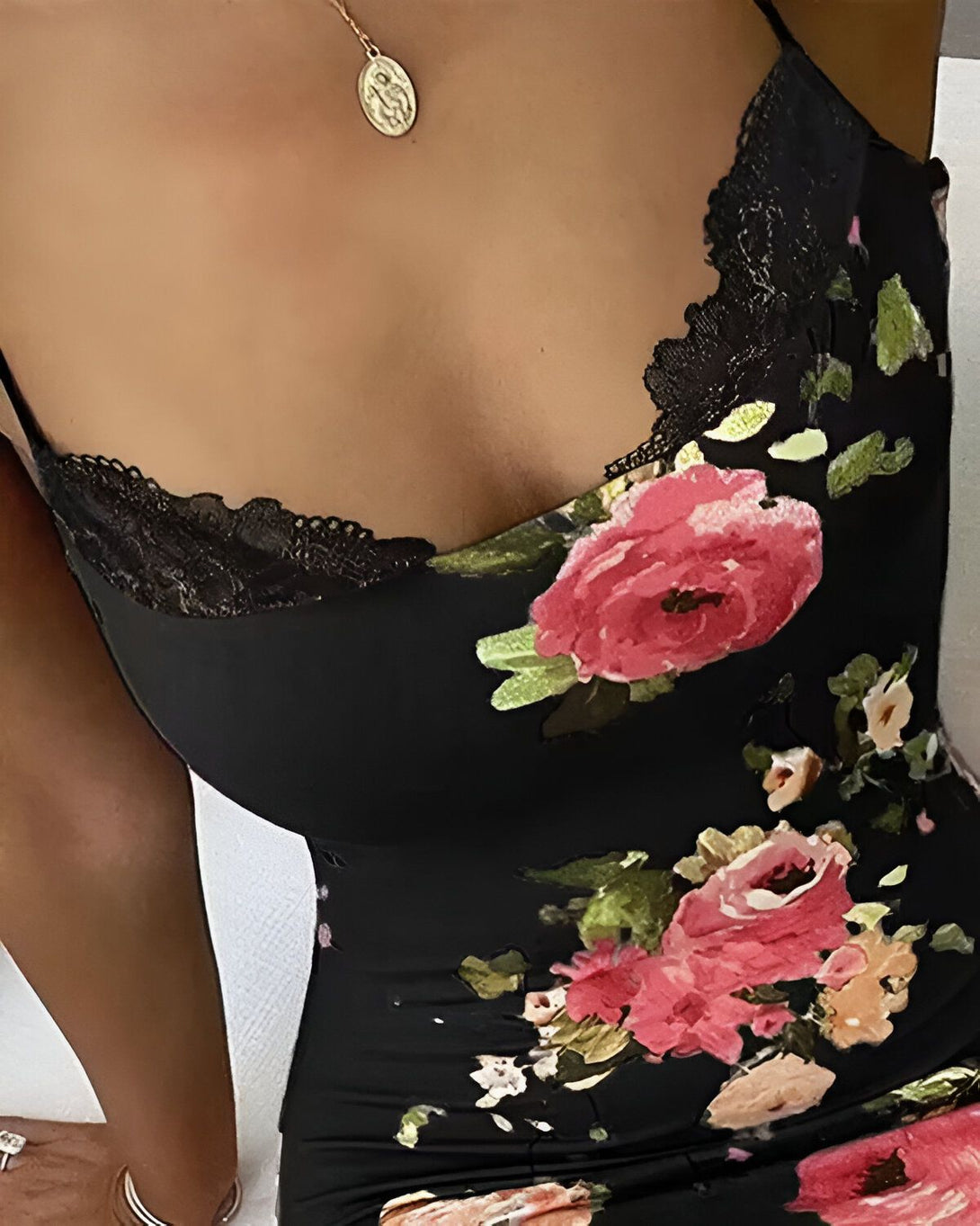 Une femme porte une robe noire à bretelles avec un décolleté en V. La robe est fleurie et possède des détails en dentelle noire.
