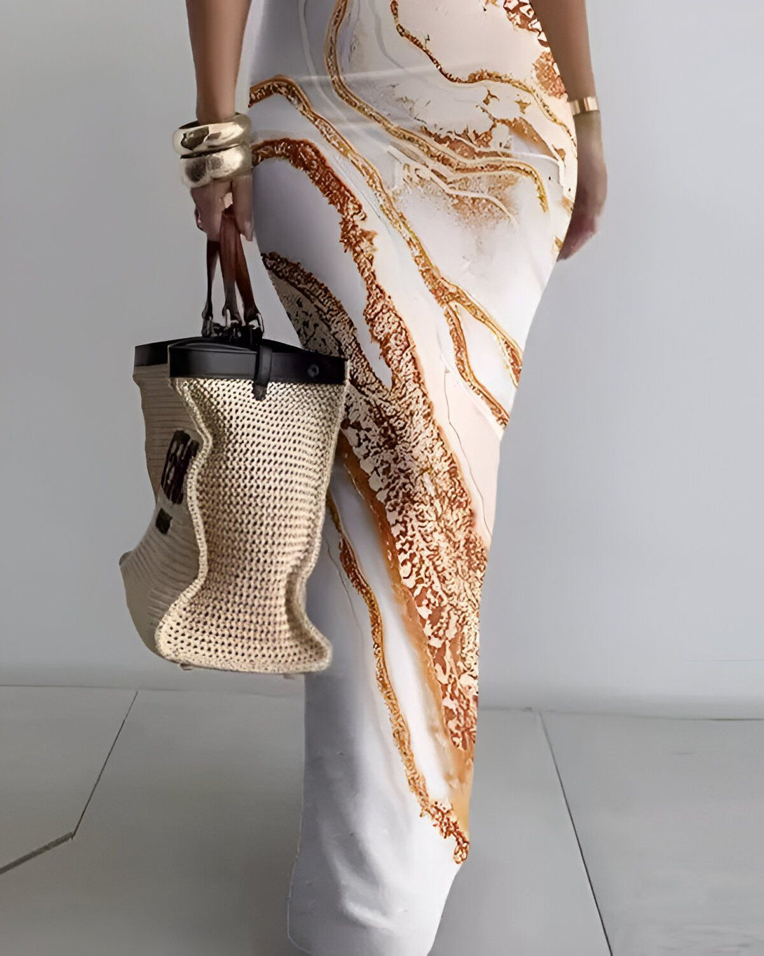 Une femme porte une robe longue moulante à imprimé marbré marron et blanc. Elle porte également un sac à main en paille beige et marron.