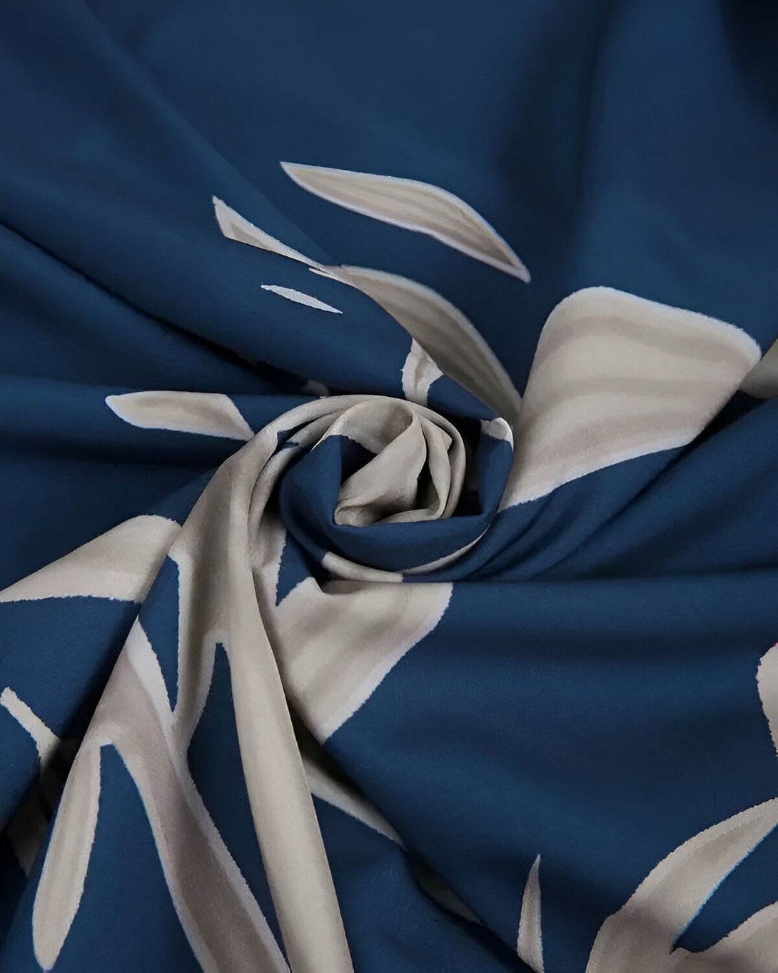 Une image d'un tissu bleu marine avec des motifs de feuilles blanches. Le tissu est froissé et on peut voir les détails du motif.