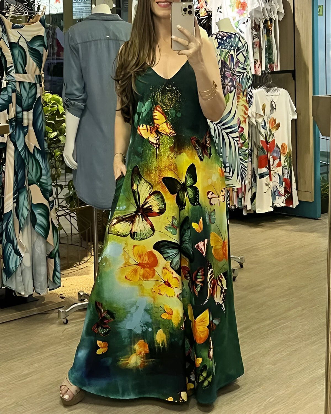 Une femme porte une robe longue verte à motifs de papillons multicolores. Elle se prend en photo dans un magasin de vêtements.