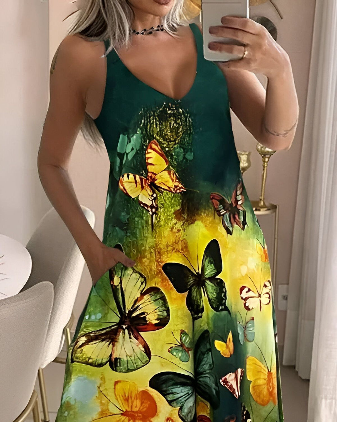 Une femme porte une robe verte à motifs de papillons multicolores. La robe est cintrée à la taille et possède des poches. La femme est blonde et porte un collier noir. Elle se prend en photo dans un miroir.