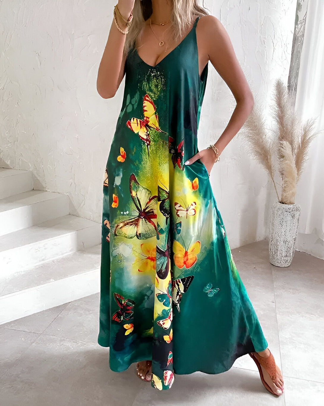 Une femme porte une robe longue verte à fines bretelles. La robe est imprimée de papillons multicolores. La femme est debout sur un sol en marbre.