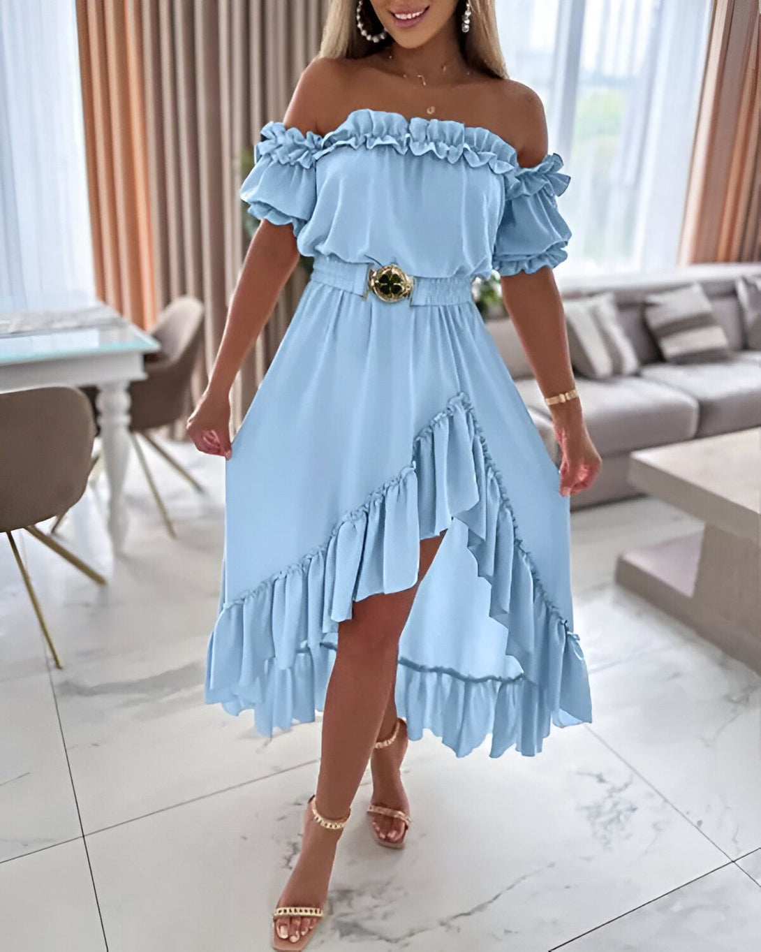 Une femme porte une robe bleu ciel à volants avec une ceinture dorée. La robe est courte devant et longue derrière. Elle porte des sandales à talons dorées.