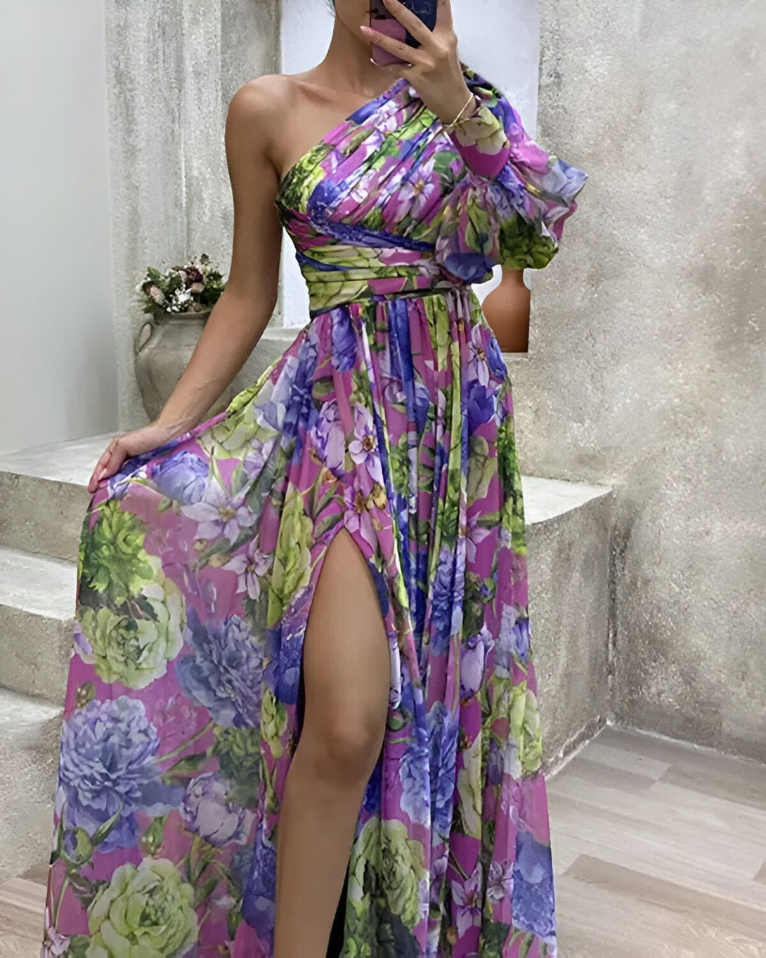 Une femme porte une robe de soirée longue et fendue sur le côté. La robe est à une épaule et est de couleur rose et verte à motifs floraux.