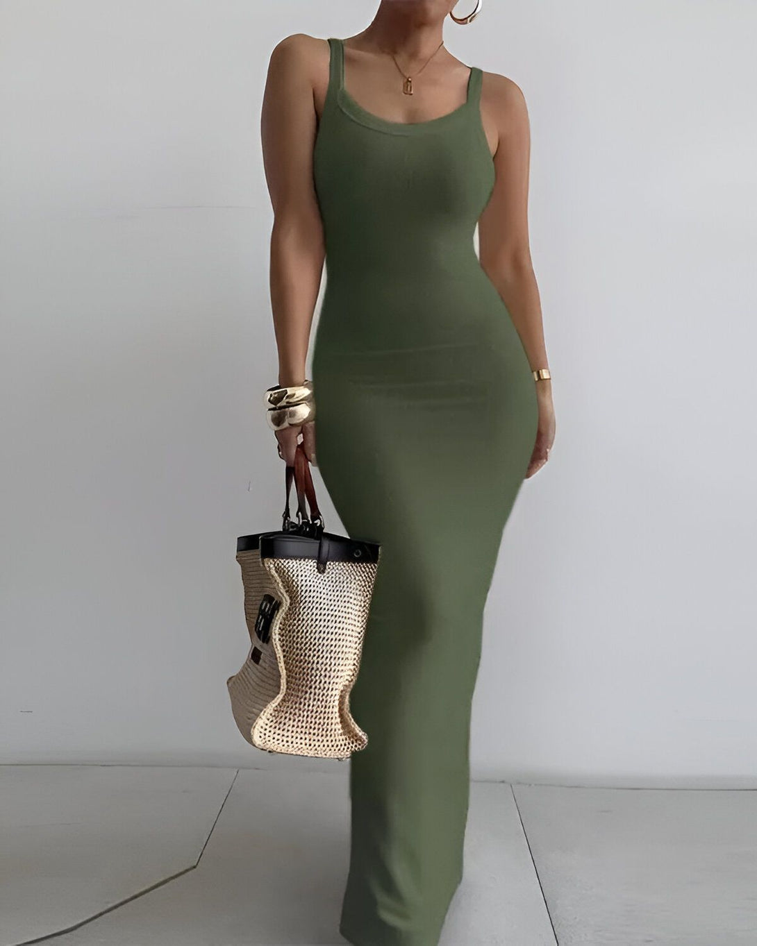 Une femme porte une robe longue verte moulante. Elle porte également un sac à main en osier marron.
