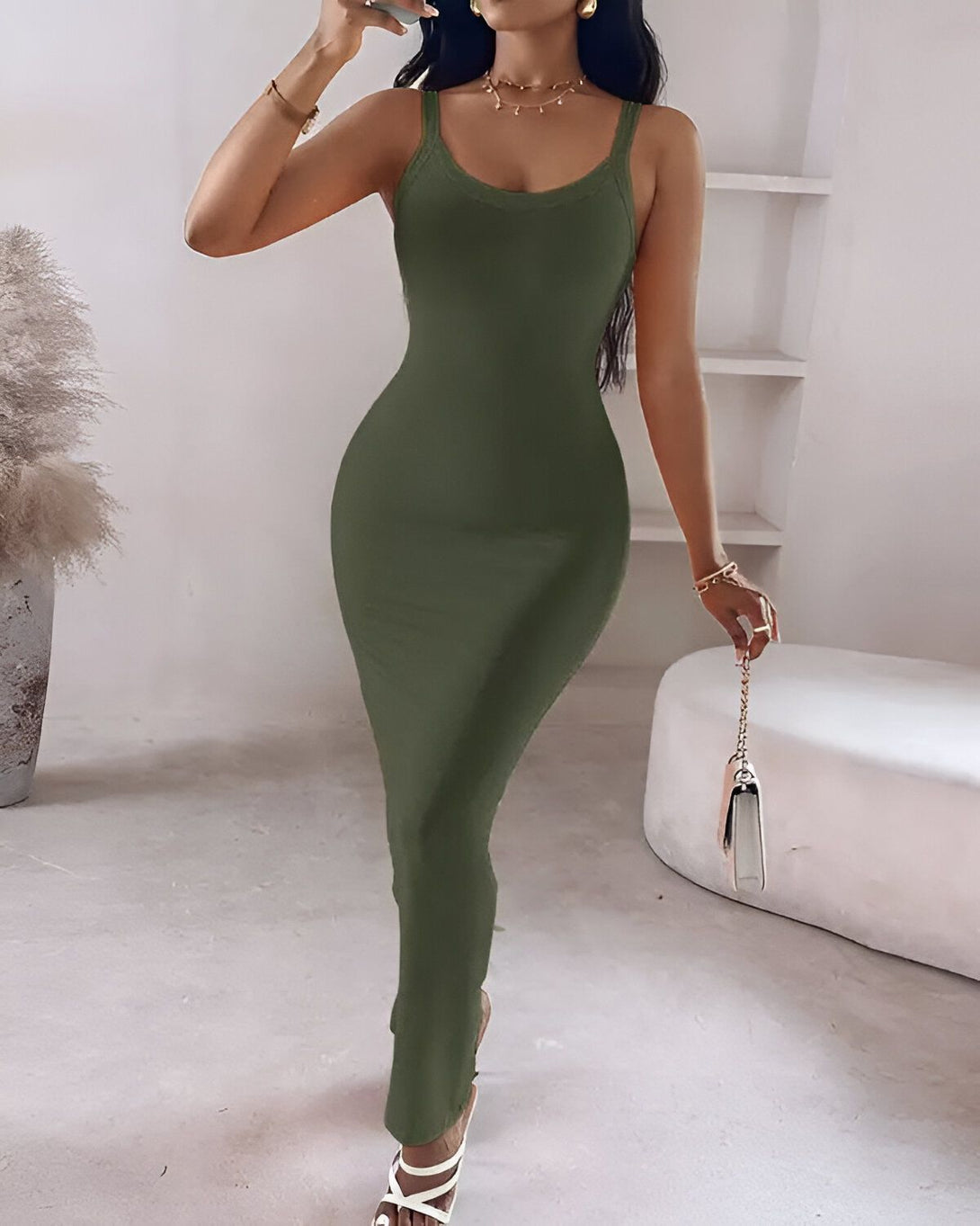 Une femme porte une robe longue verte moulante. Elle est dos à la caméra et porte des sandales à talons transparentes. Ses cheveux sont longs et noirs et elle a un maquillage léger.