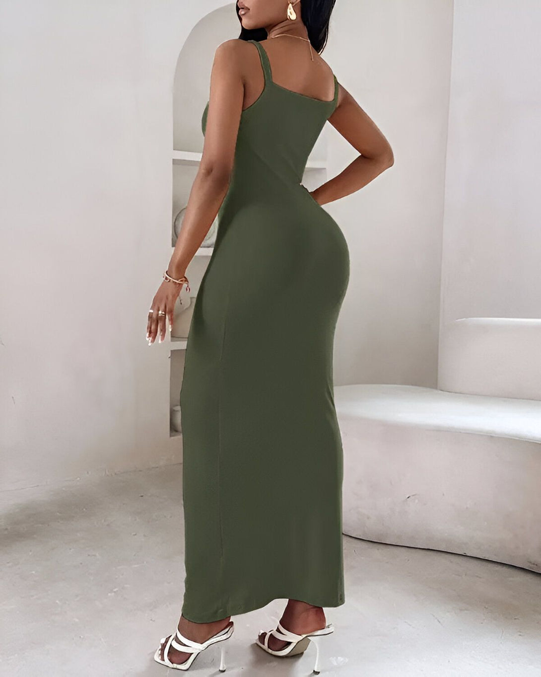 Une femme porte une robe longue moulante vert olive avec des sandales à talons blanches.