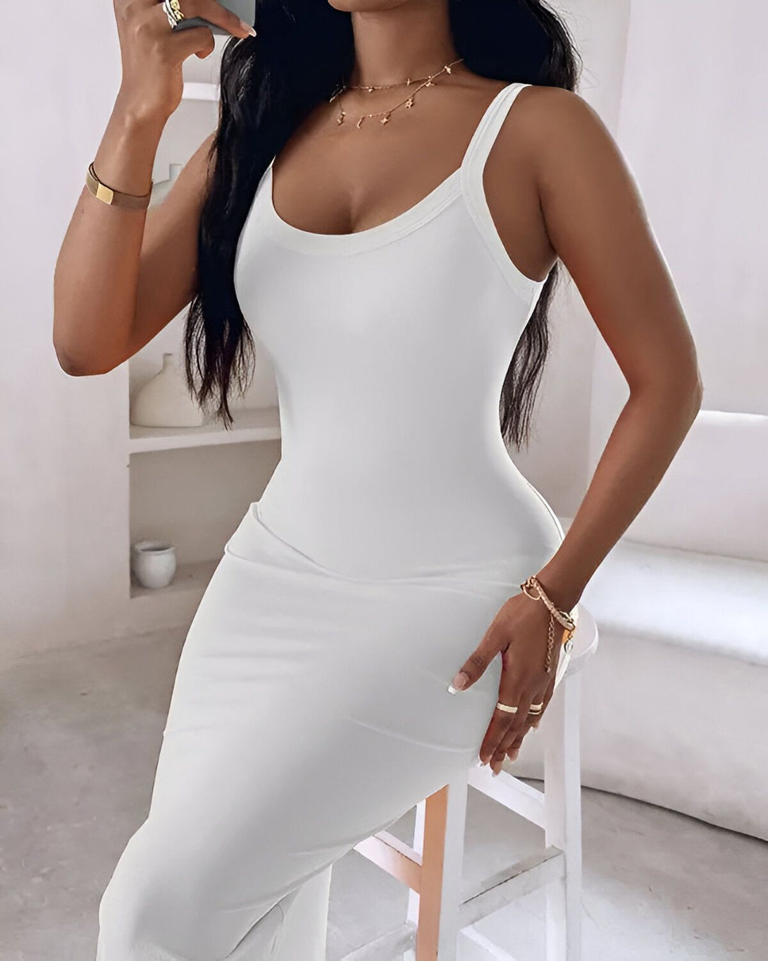 Une femme porte une robe blanche moulante. Elle est debout, de profil, et tient un téléphone portable à la main. Ses cheveux sont longs et noirs.