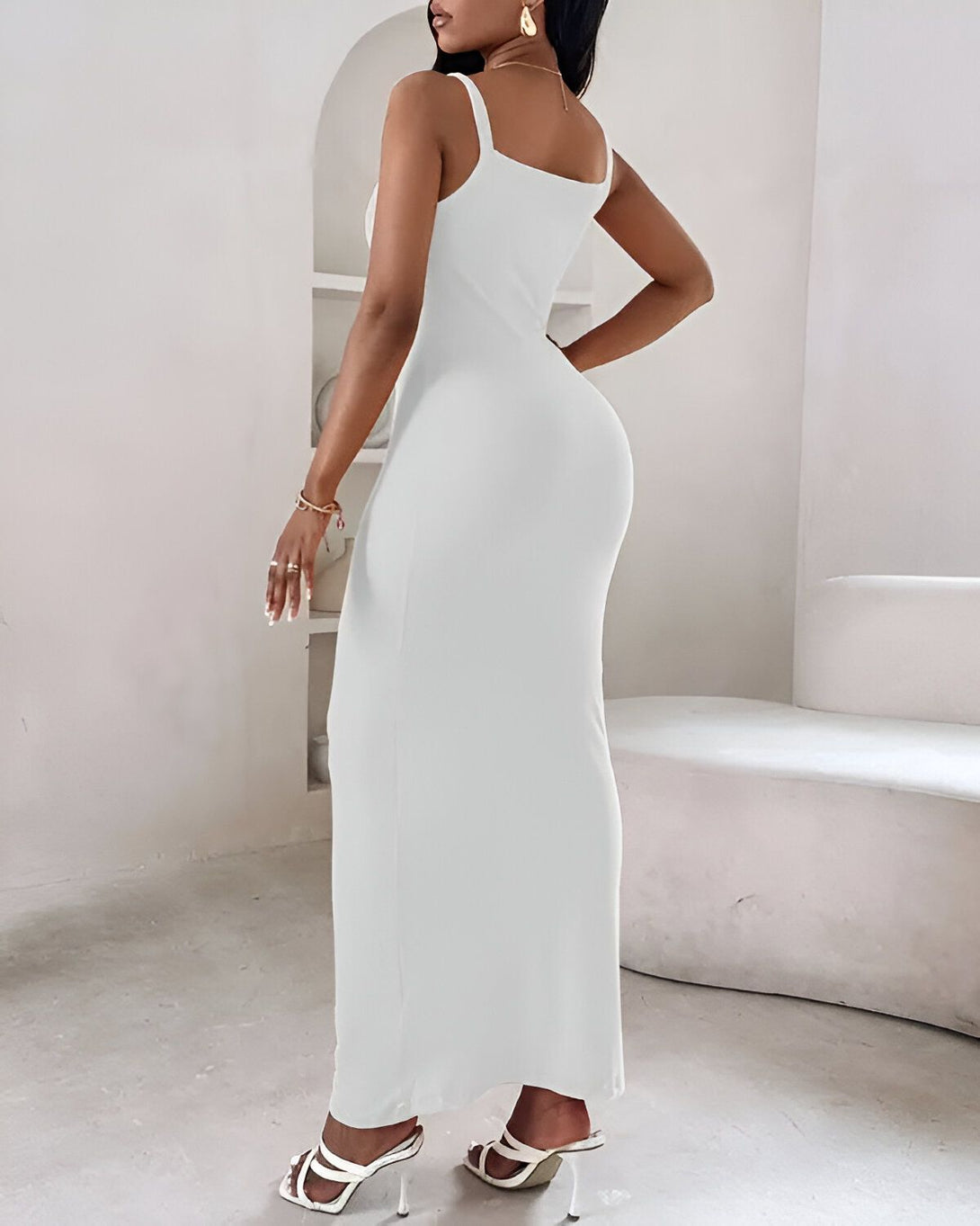 Une femme porte une robe blanche moulante longue avec des talons blancs.