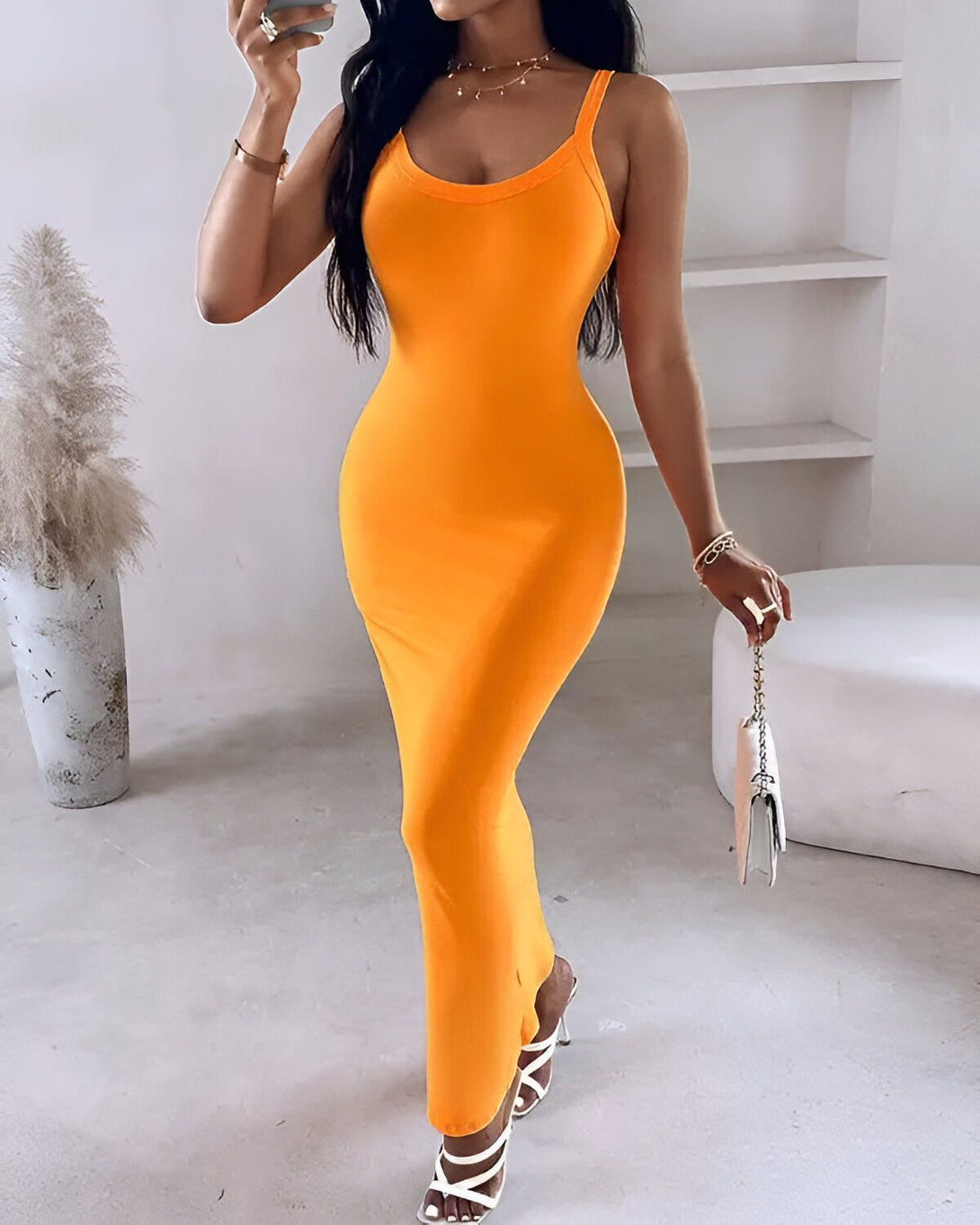 Une femme porte une robe longue orange moulante. Elle est dos à la caméra et porte des talons blancs. Ses cheveux sont longs et noirs.
