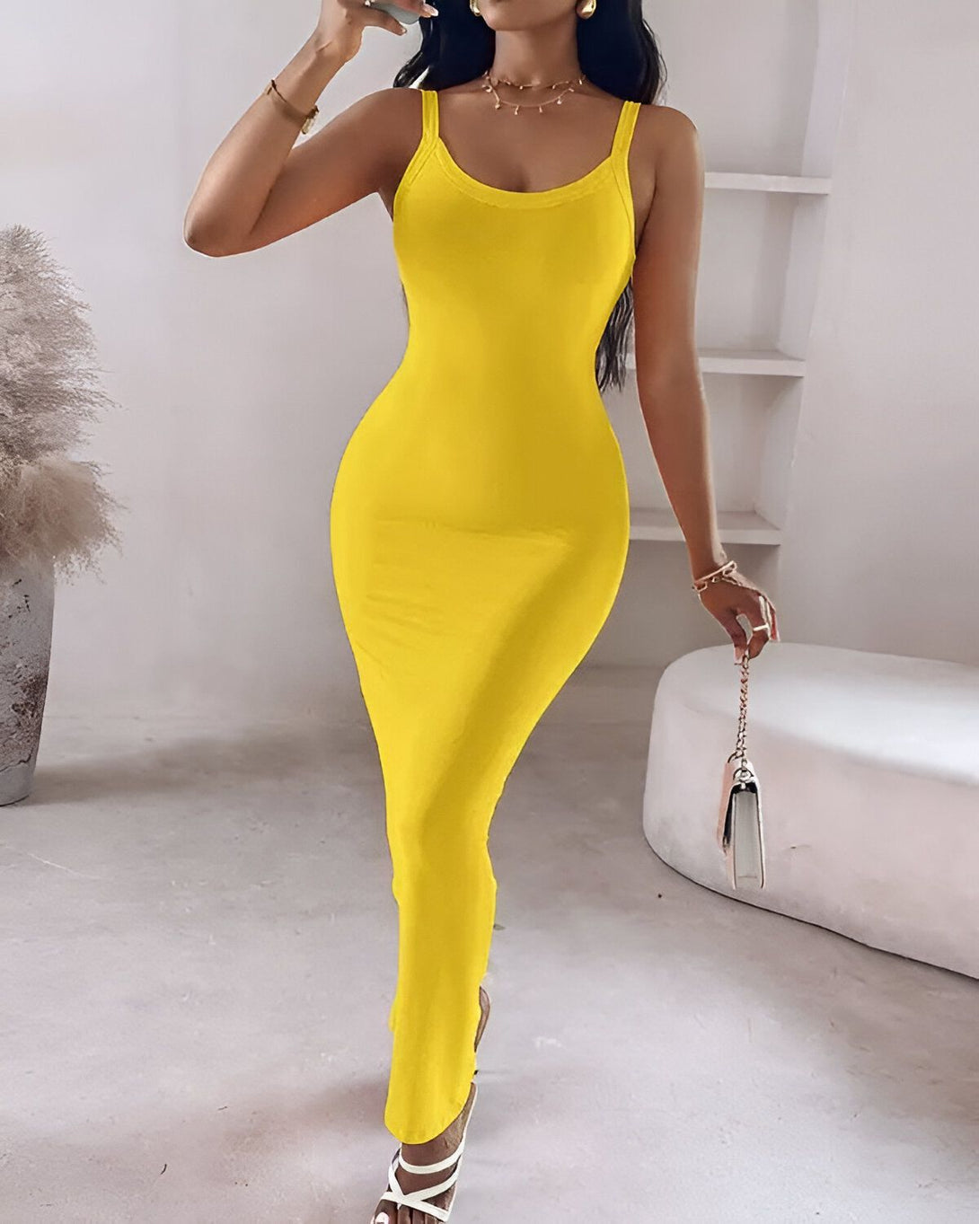 Une femme porte une robe jaune moulante longue. Elle est dos à la caméra et porte des sandales à talons transparentes. Ses cheveux sont longs et noirs.