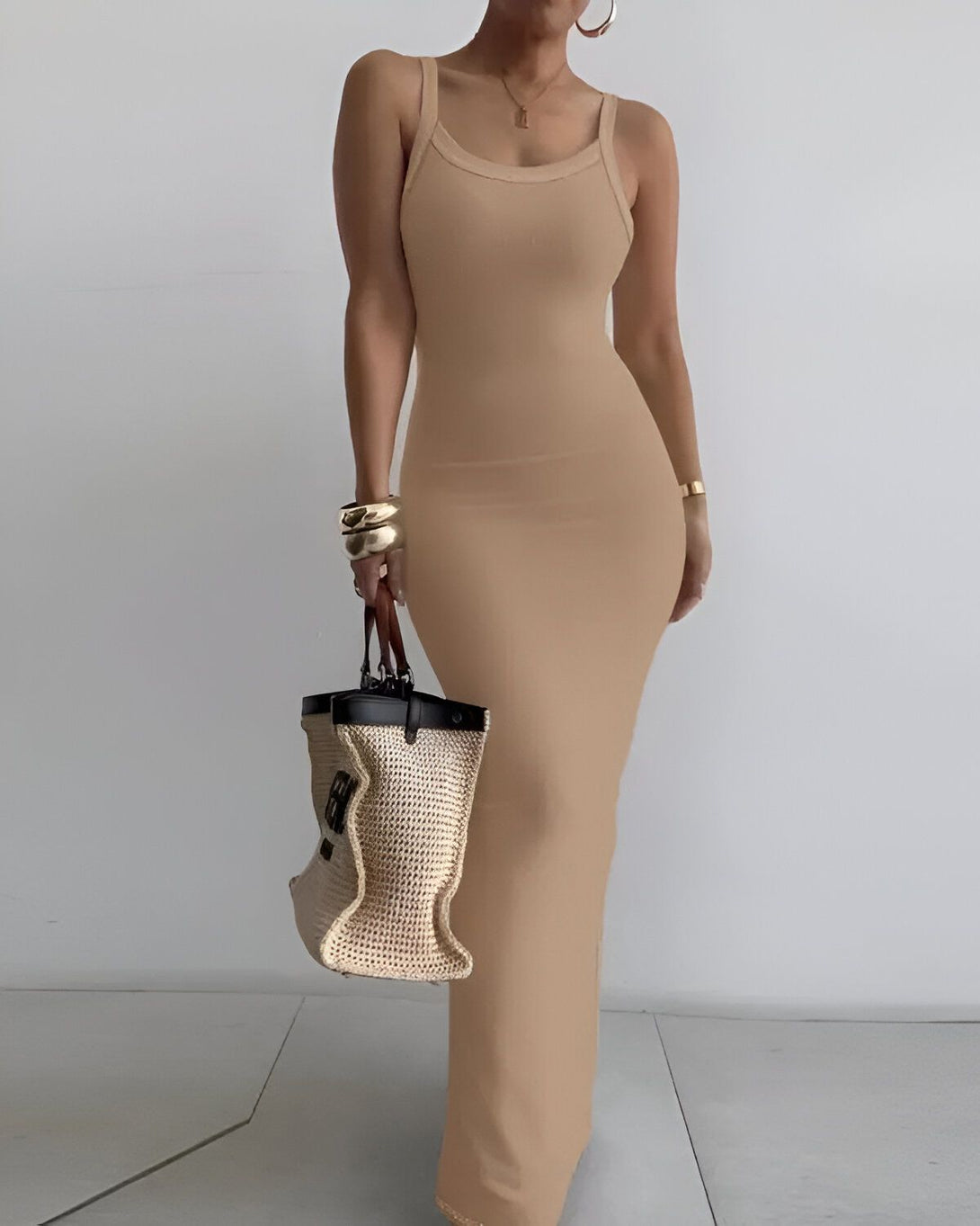Une femme porte une robe longue beige moulante et un sac à main marron.
