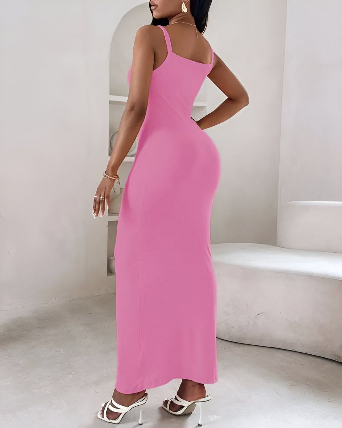 Une femme porte une robe longue rose moulante. La robe est fendue sur le côté. La femme est vue de dos.