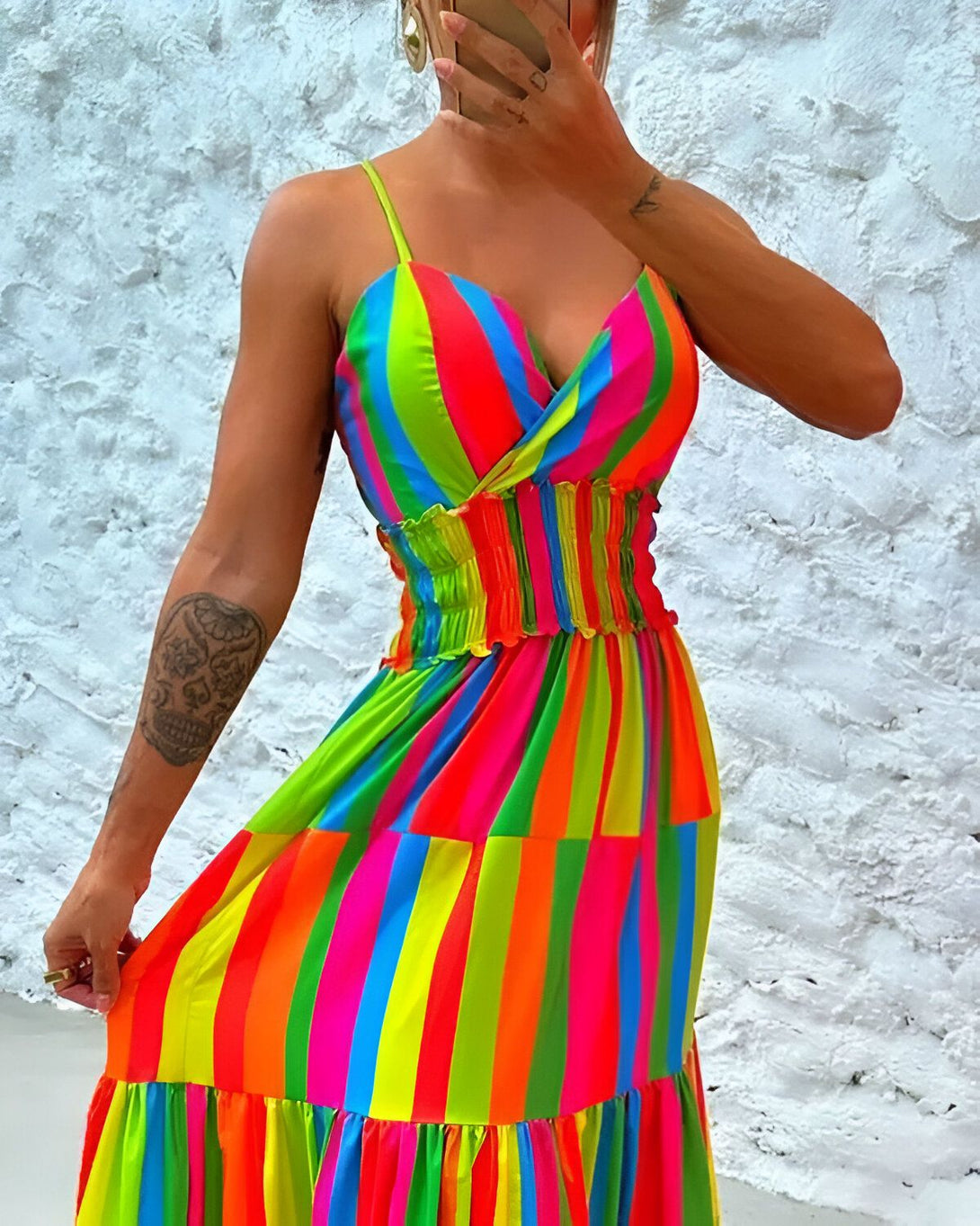 Une femme porte une robe longue à fines bretelles, cintrée à la taille, avec un motif à rayures verticales de différentes couleurs vives.