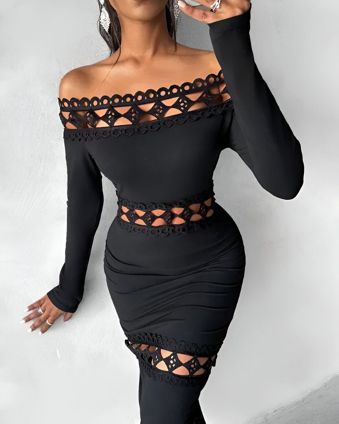 Une femme porte une robe noire moulante avec des découpes au niveau des épaules et de la taille. La robe est fendue sur le côté.