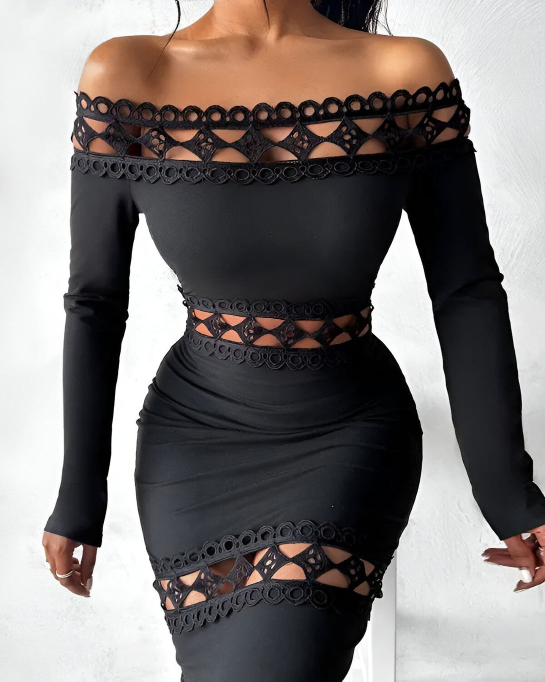 Une femme porte une robe noire moulante avec des découpes au niveau des épaules et de la taille. La robe est en dentelle et a un col Bardot.