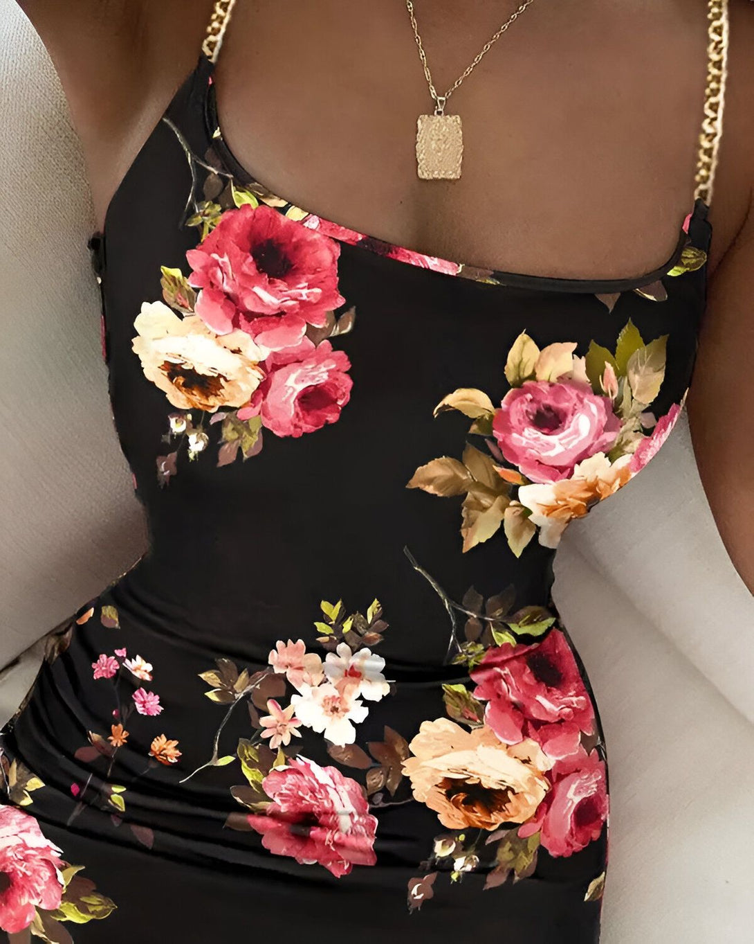 Une femme porte une robe noire moulante à fleurs roses et rouges. Elle porte également un collier doré.