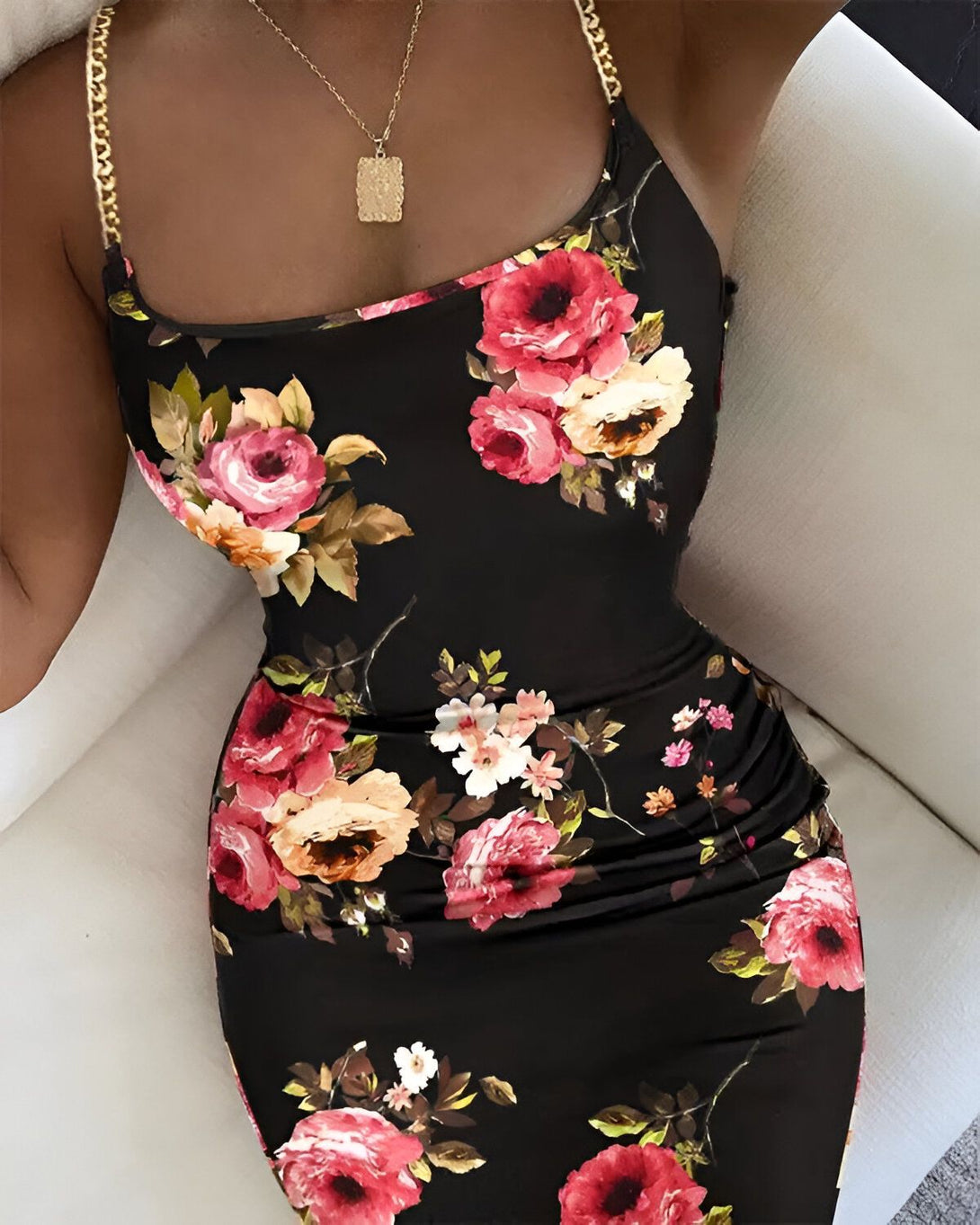 Une femme porte une robe noire moulante à fleurs rouges et roses. Elle porte également un collier avec un pendentif doré.