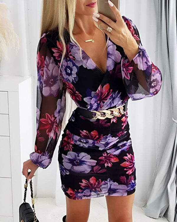 Une femme porte une robe moulante à fleurs violettes et noires. La robe a un décolleté en V et des manches longues. La femme porte également une ceinture dorée.